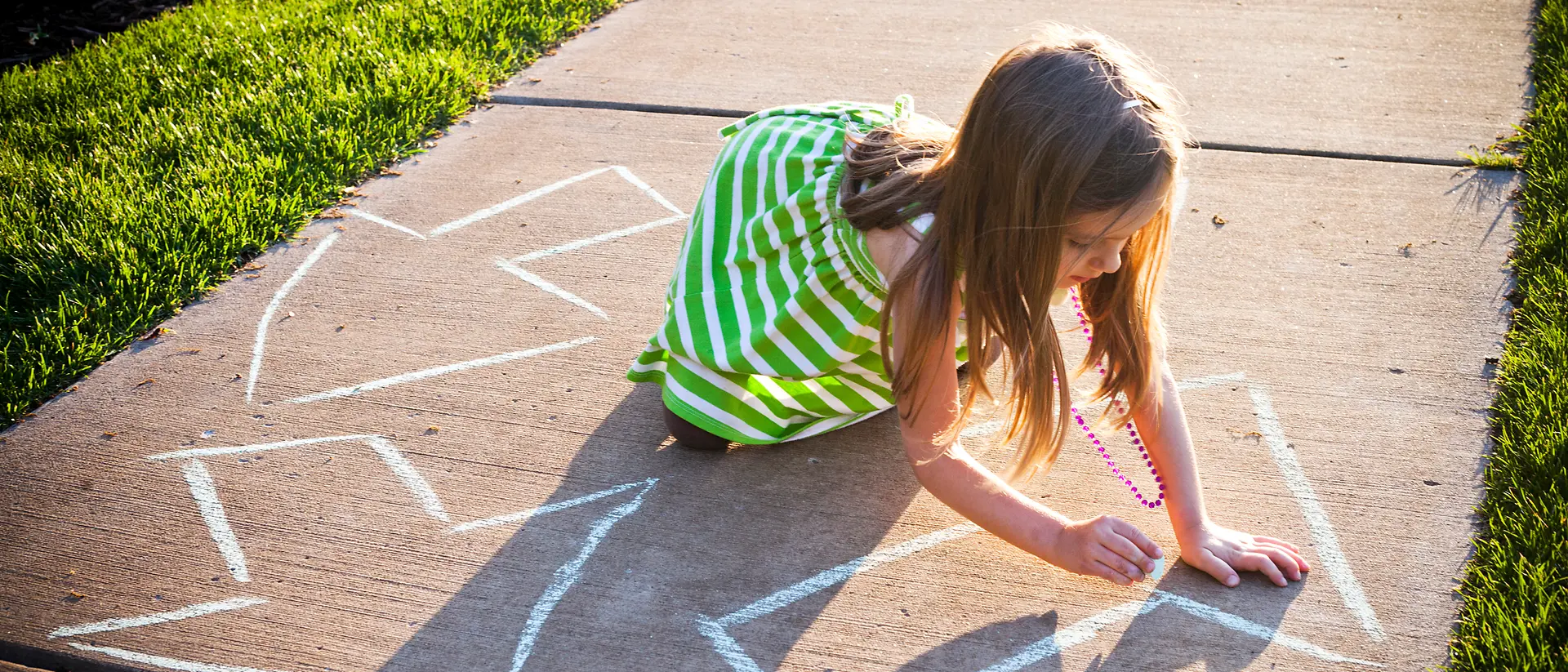 Menina com vestido às riscas verde e branco a desenhar com giz setas no chão 